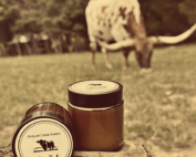 Recommended Alt Text: Handcrafted tallow balm jar and natural bar soap with a decorative wooden cow on a rustic surface.