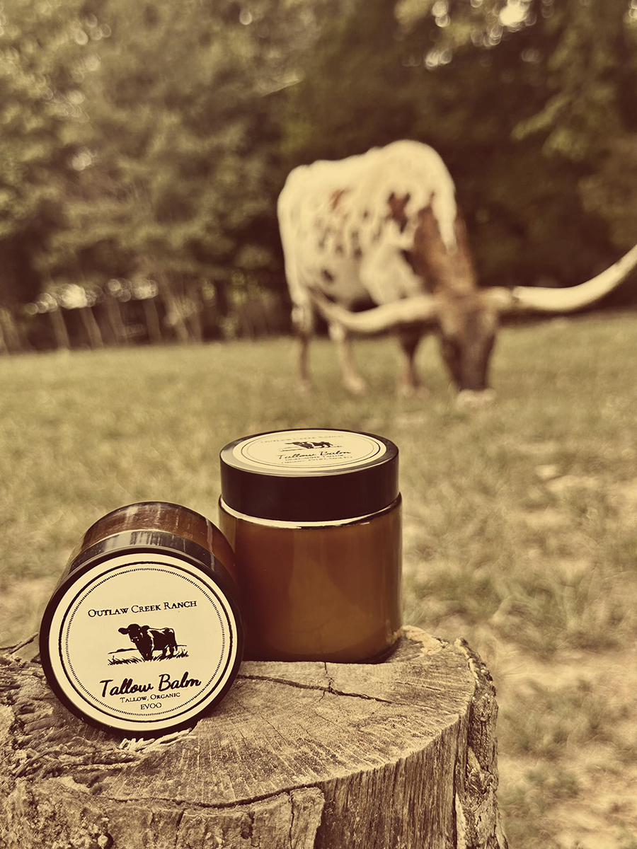 Recommended Alt Text: Handcrafted tallow balm jar and natural bar soap with a decorative wooden cow on a rustic surface.